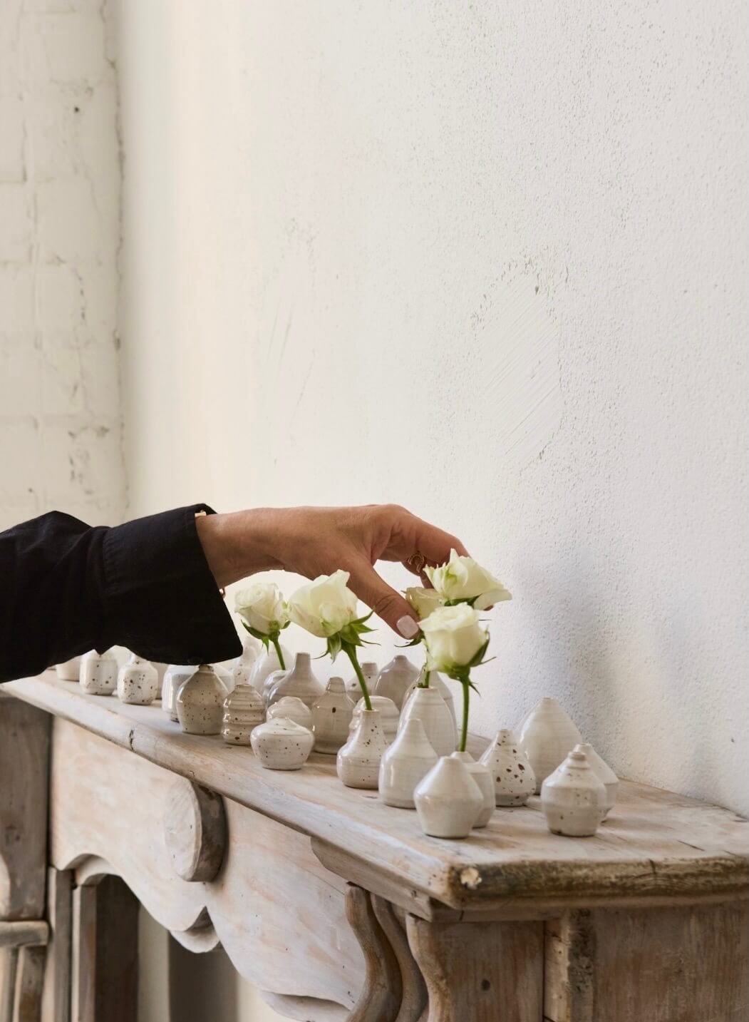 Hand arranging white flowers in small ceramic vases on a wooden table.