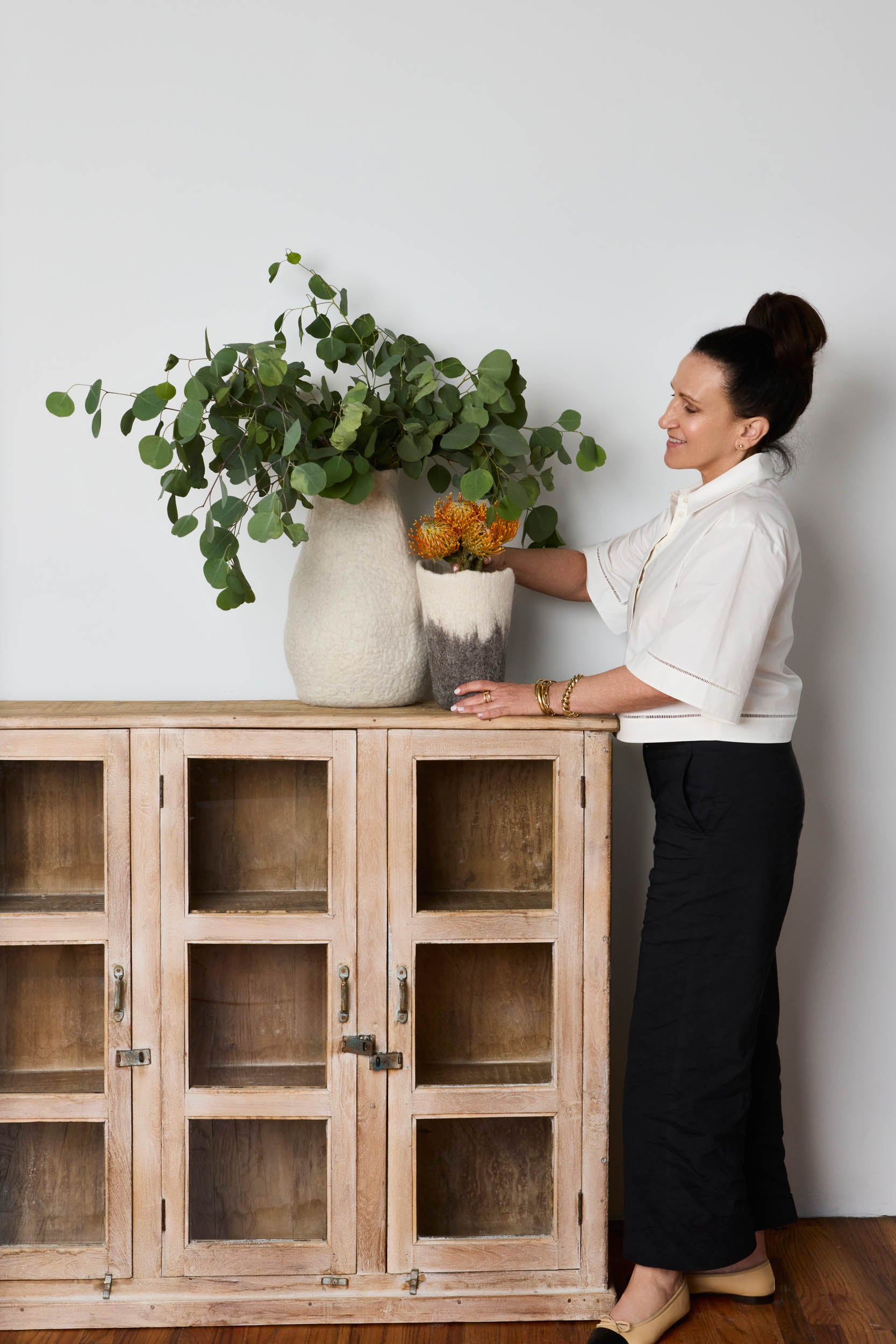 Michelle Lisa arranging plants on a wooden cabinet against a white wall
