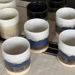 Set of ceramic cups with blue and brown stripes on a textured surface.
