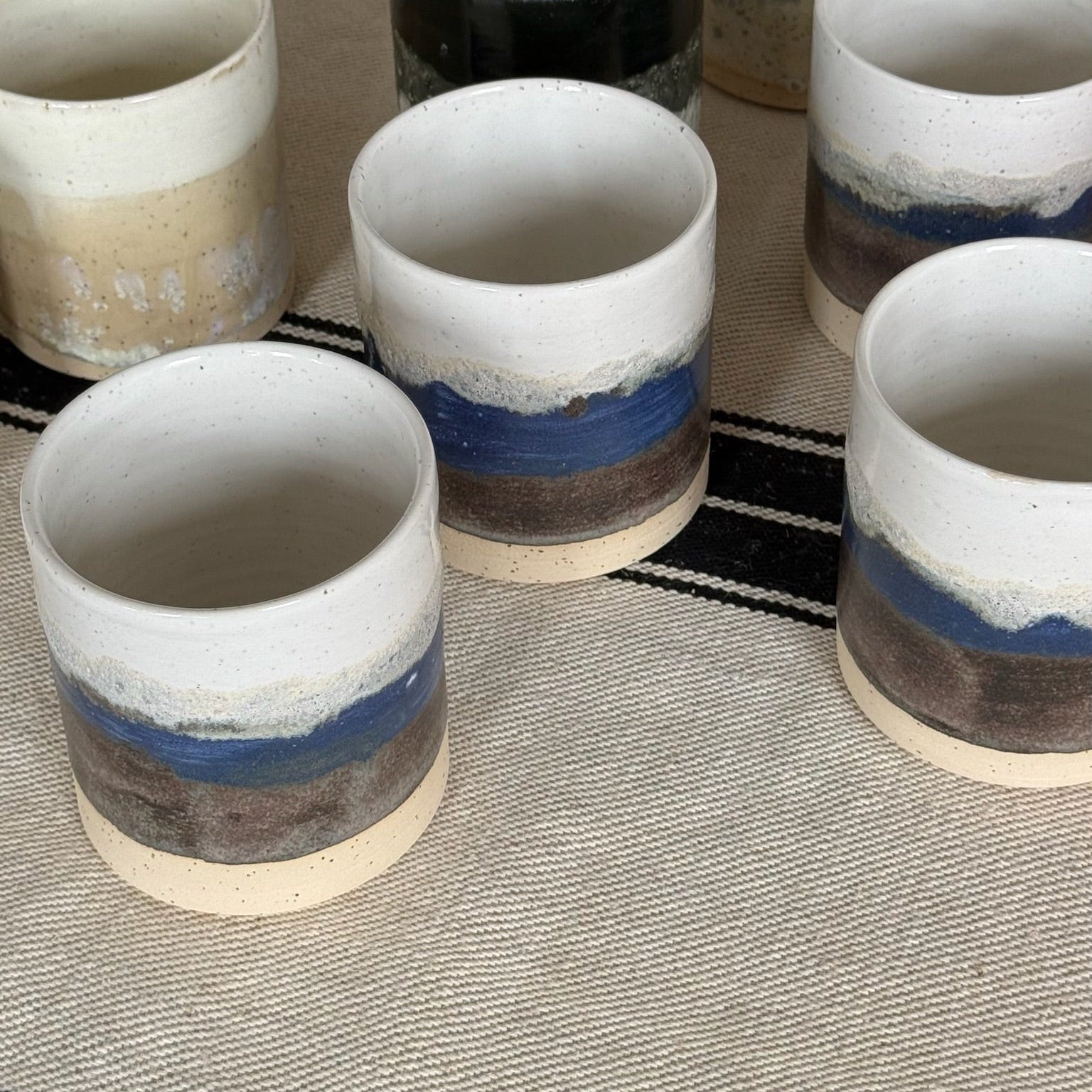 Set of ceramic cups with blue and brown stripes on a textured surface.