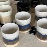 Set of ceramic cups with blue and brown stripes on a textured surface.