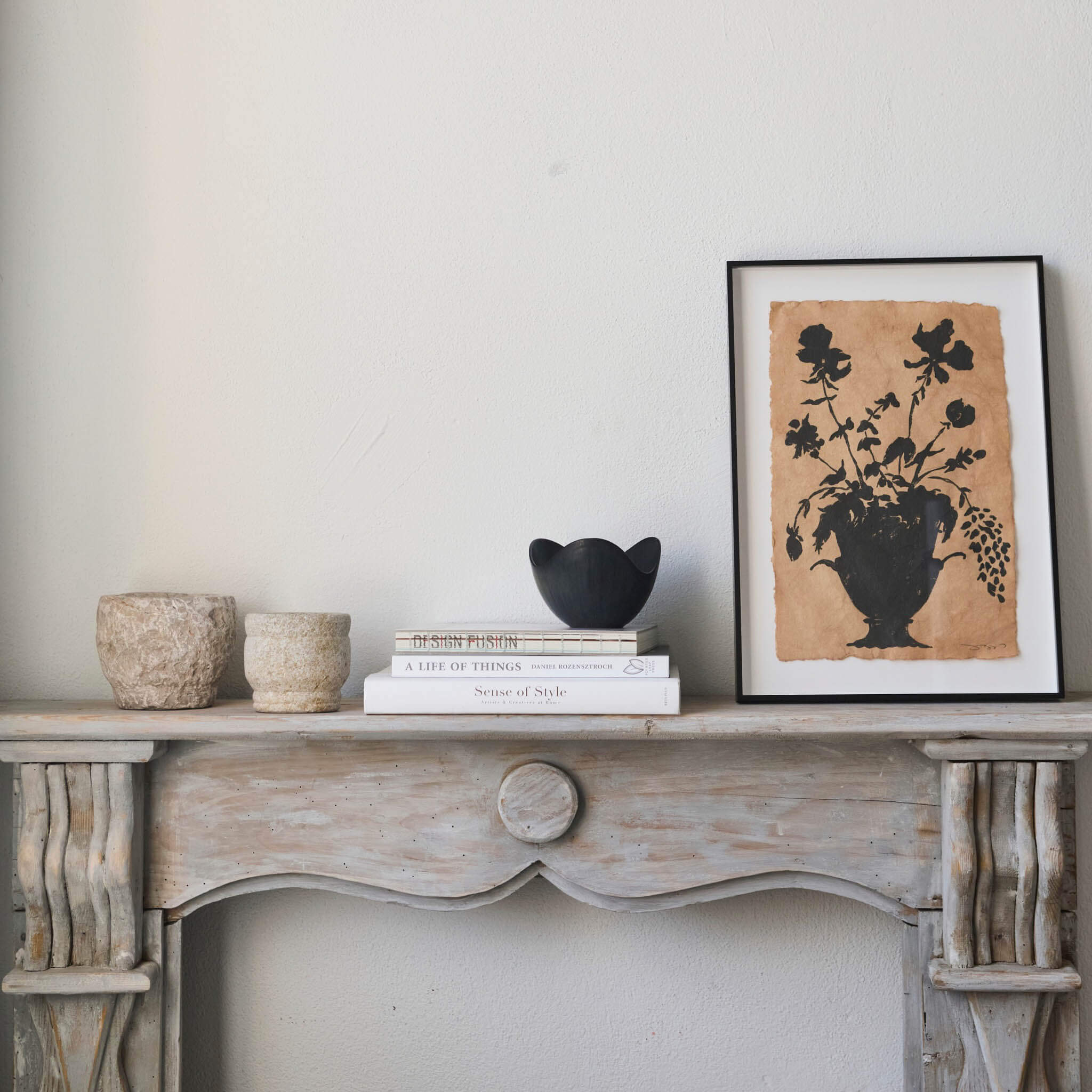 Decorative mantle with books, bowls, and a framed print on a neutral wall.
