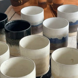 Collection of ceramic cups on a table with oranges in the background.