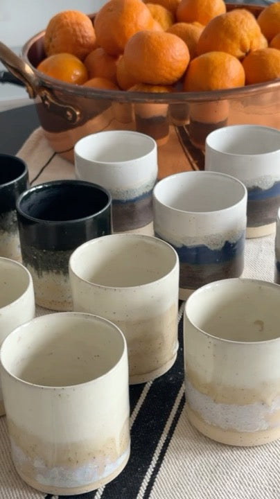 Collection of ceramic cups on a table with oranges in the background.