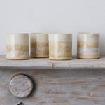 Four ceramic candles with a gradient finish on a wooden shelf against a light background