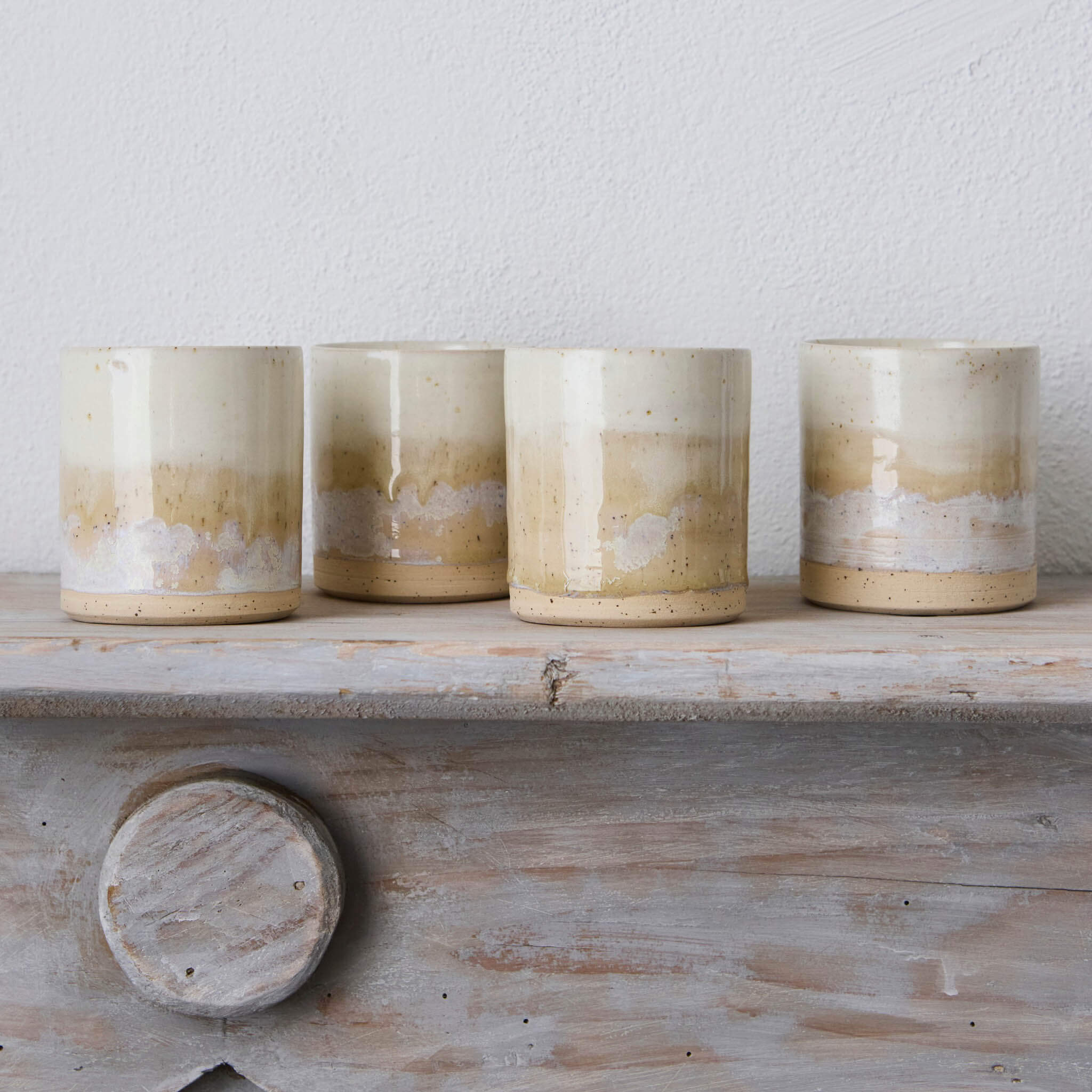 Four ceramic candles with a gradient finish on a wooden shelf against a light background