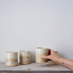 Hand holding a ceramic cup on a wooden surface with a plain background