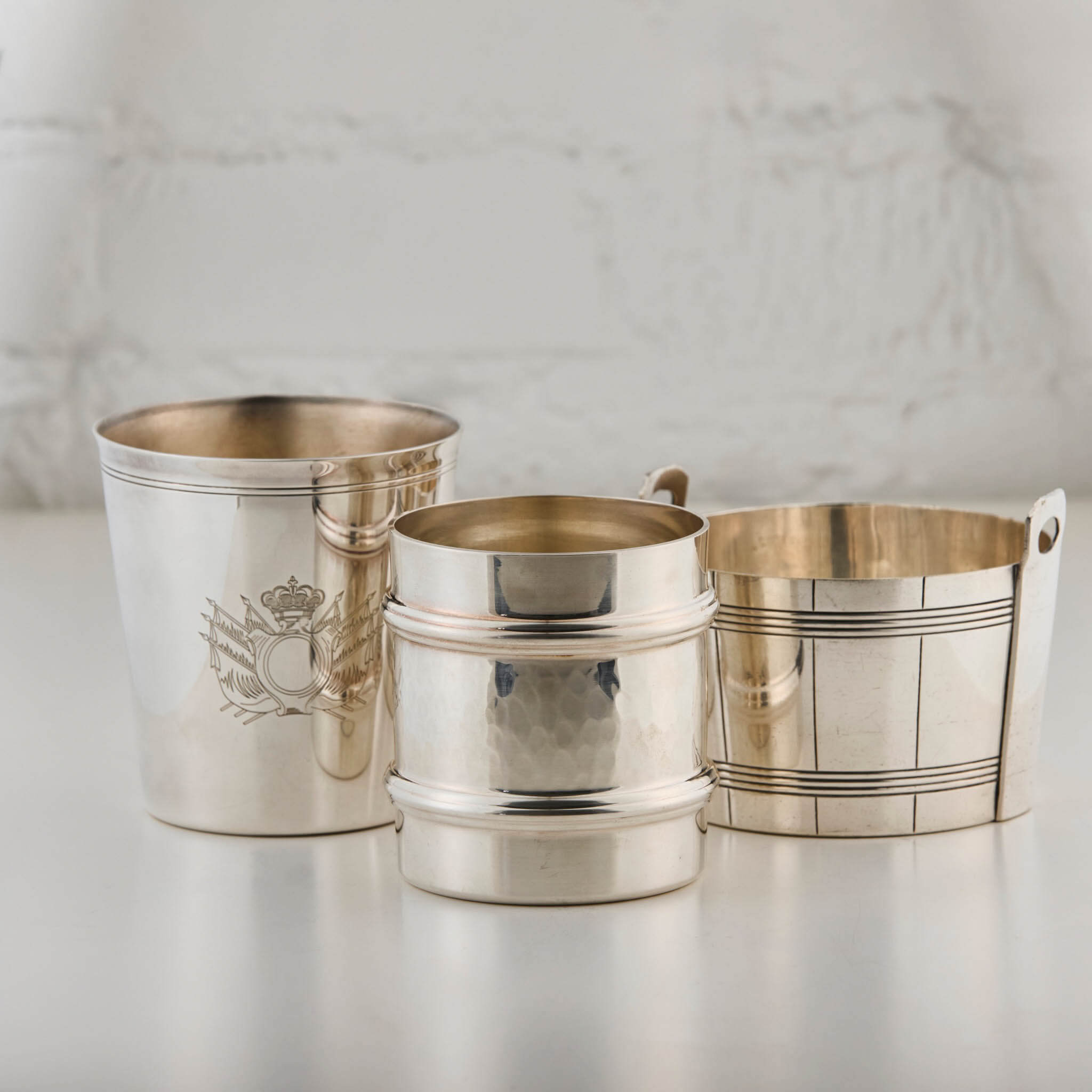 Two silver cups and a silver ice bucket with different designs on a light background