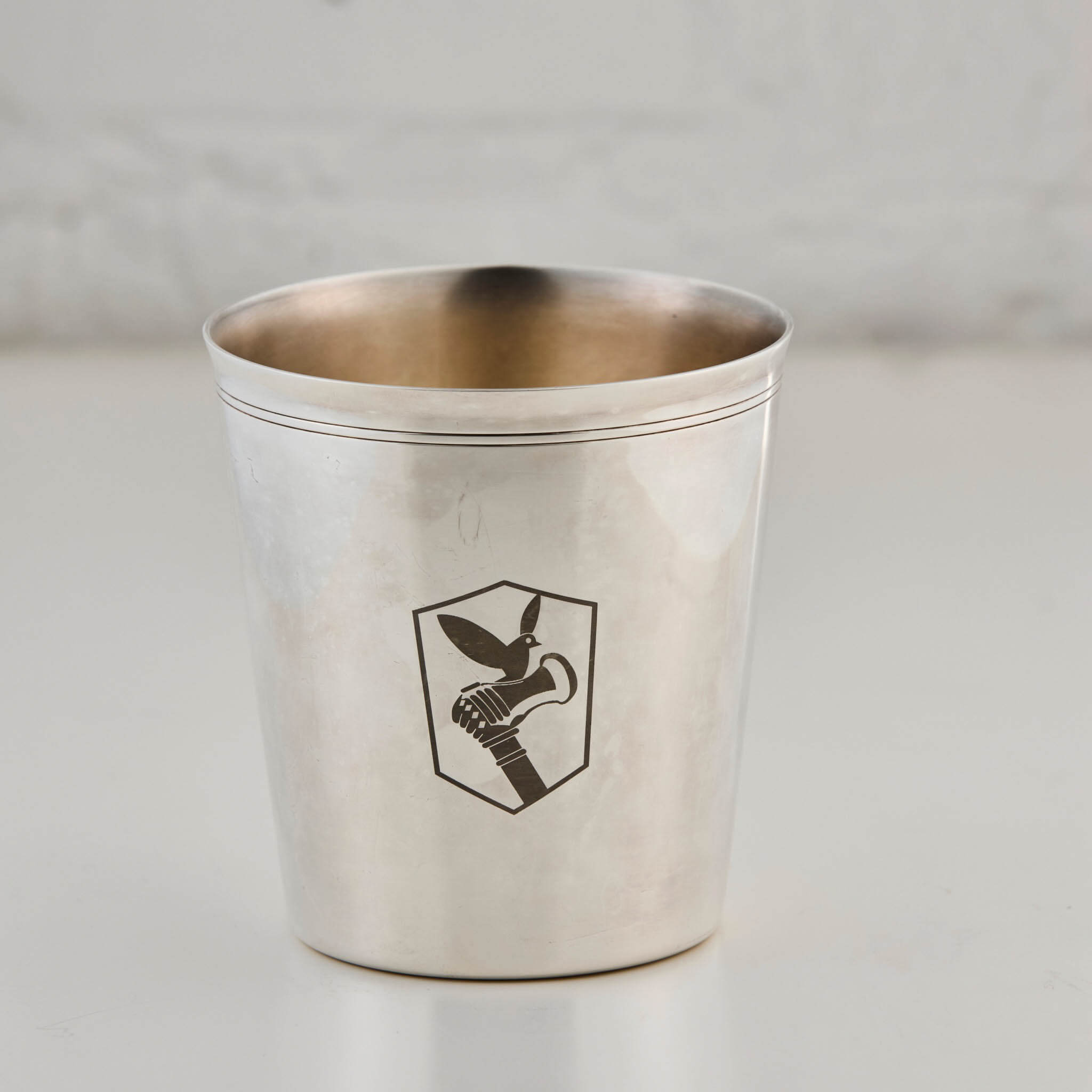 Silver cup with an engraved logo on a light gray background