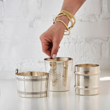 Hand holding a silver cup with another silver cup and a silver ice bucket on a light background