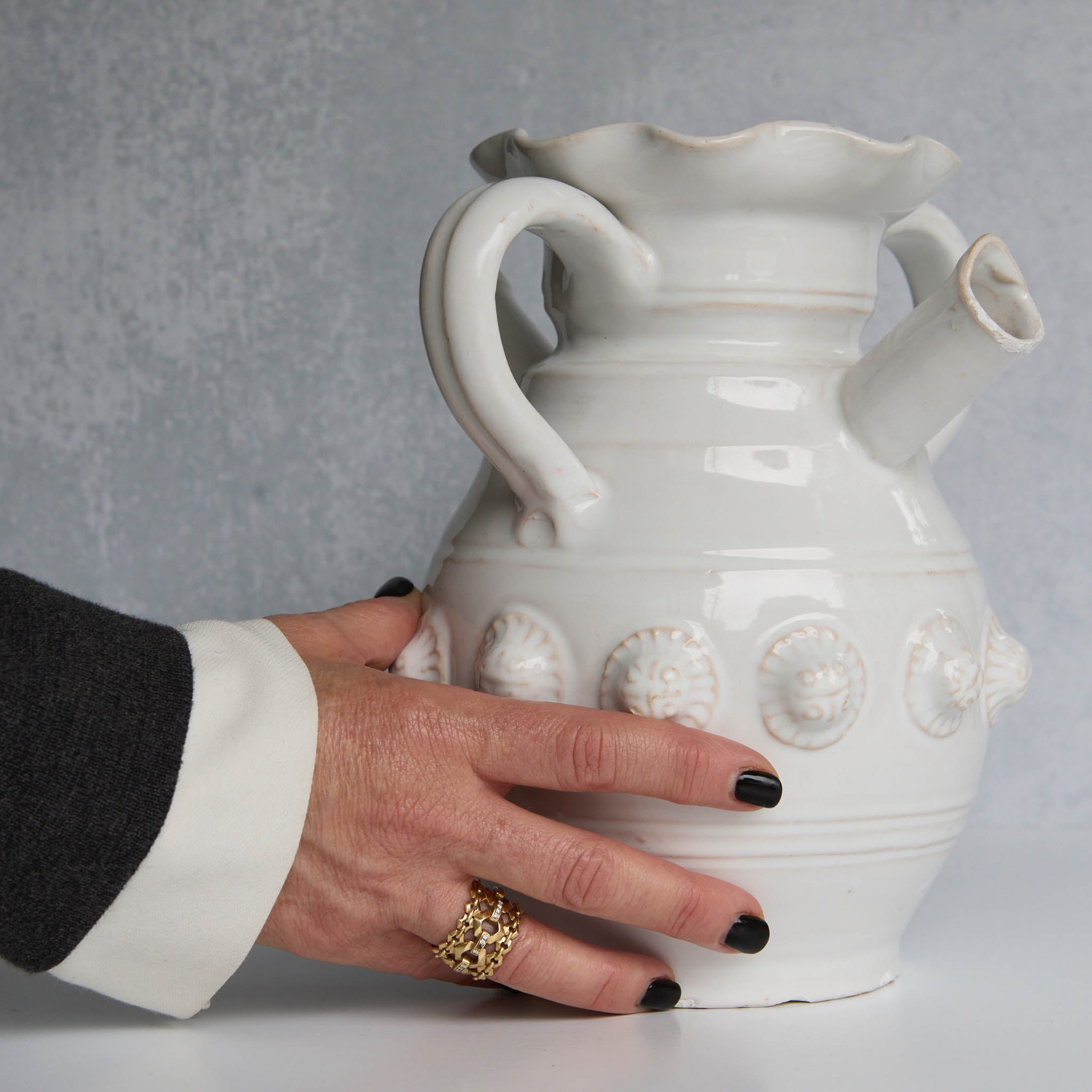 White ceramic pitcher with decorative elements held by a hand against a gray background