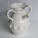 White ceramic pitcher with handles and decorative elements on a gray background