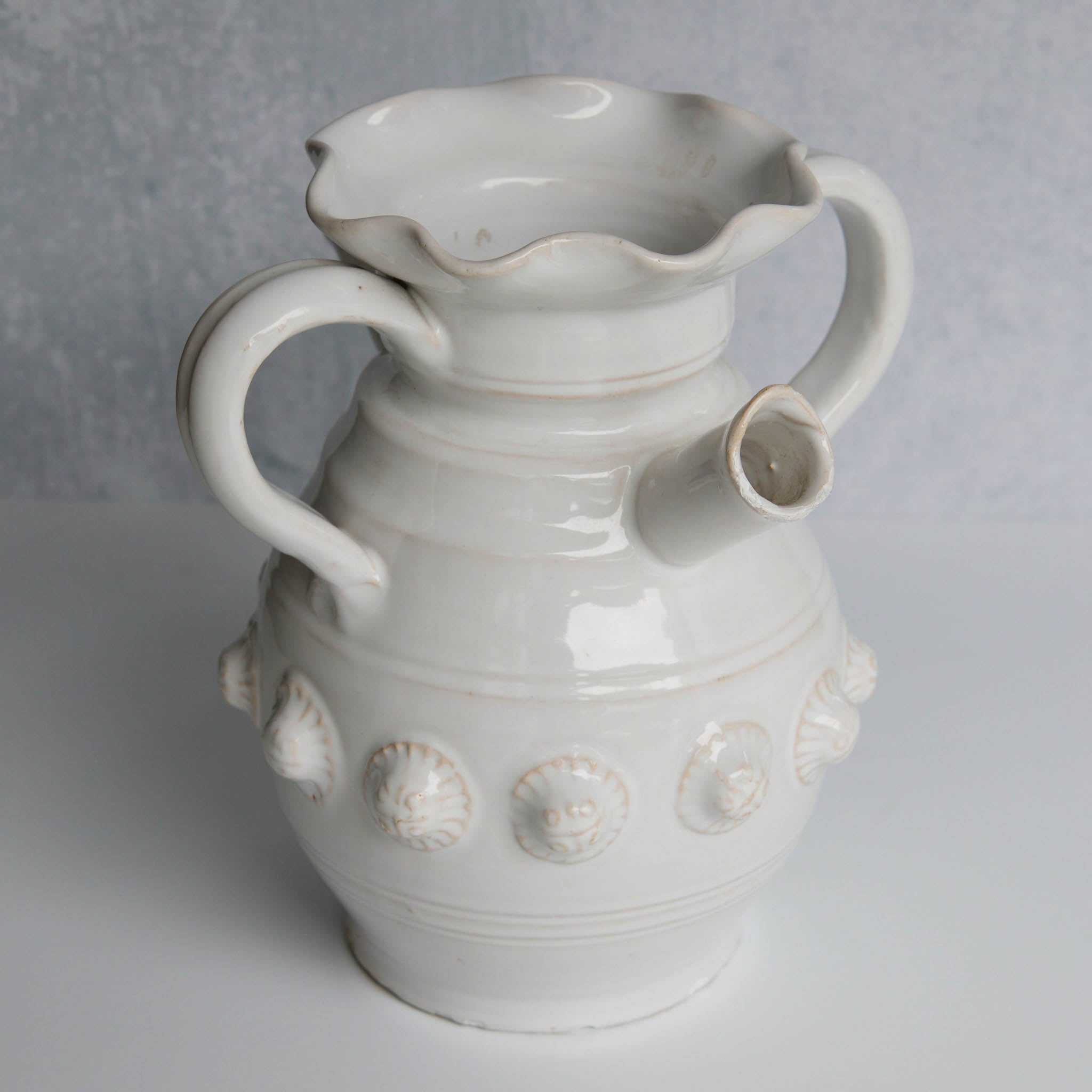 White ceramic pitcher with handles and decorative elements on a gray background
