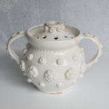 White ceramic vessel with removable lid with textured surface on a gray background