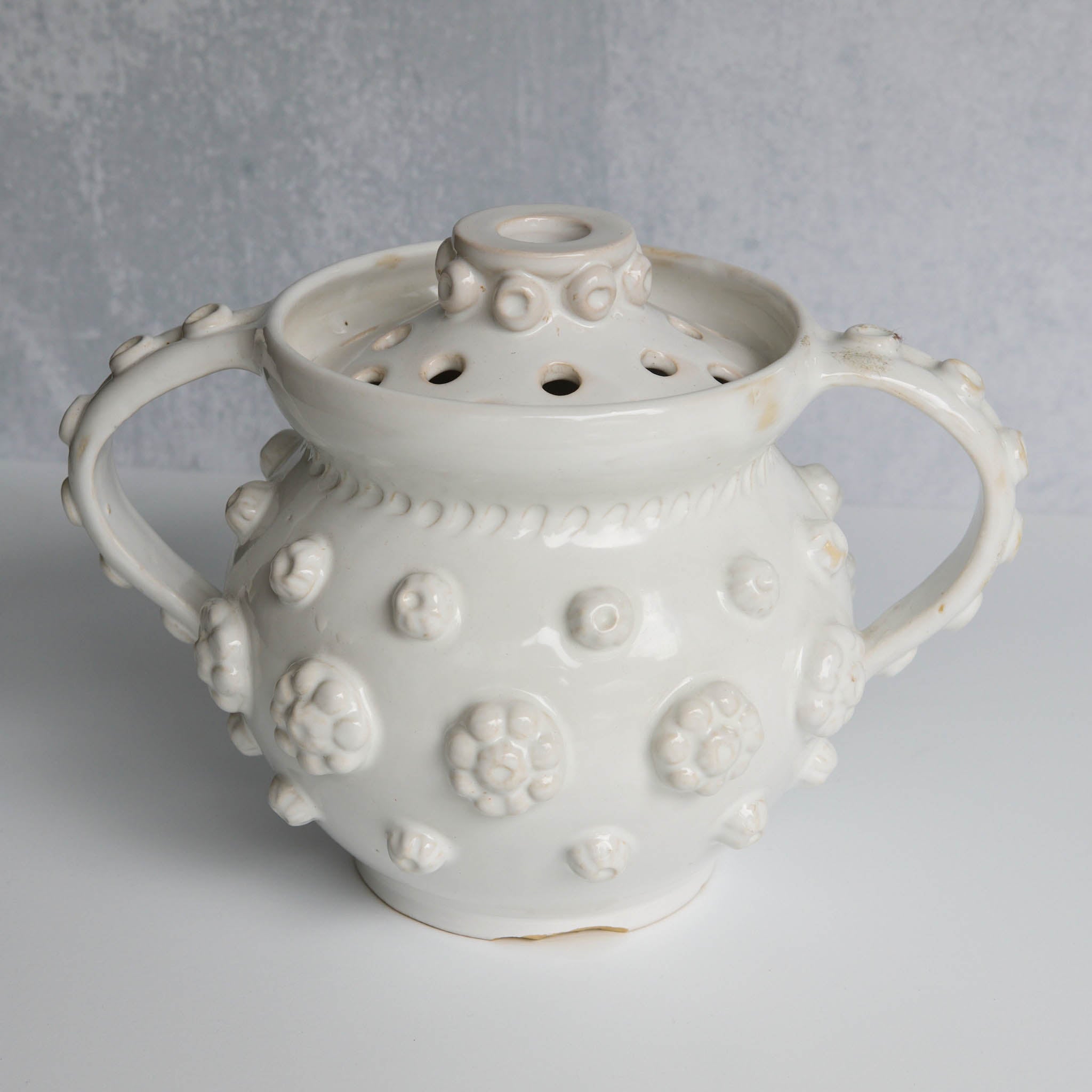 White ceramic vessel with removable lid with textured surface on a gray background