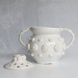 White ceramic vase with removable lid with floral patterns on a gray background