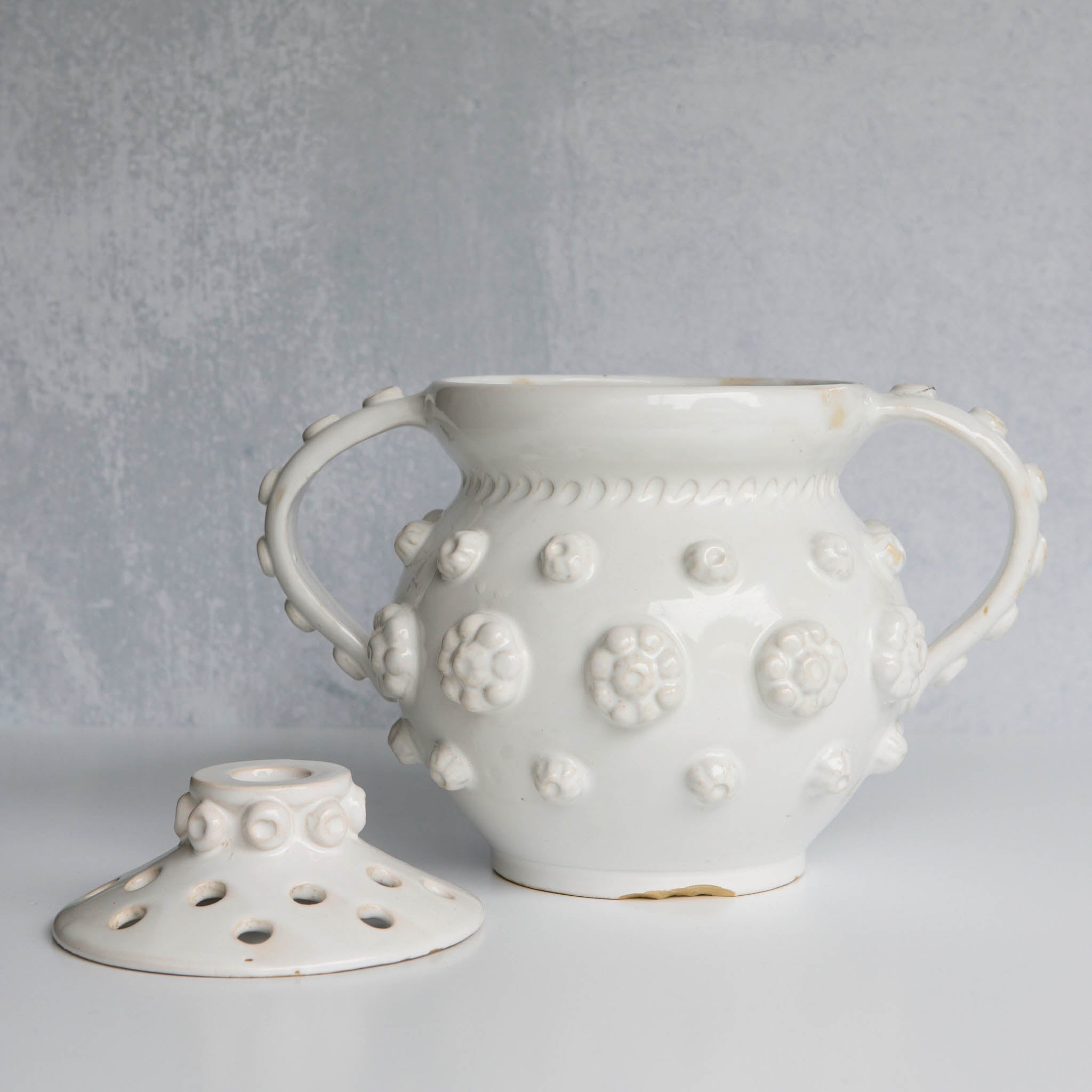 White ceramic vase with removable lid with floral patterns on a gray background