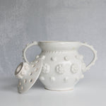 White ceramic vessel with removable lid with floral patterns on a gray background