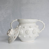 White ceramic vessel with removable lid with floral patterns on a gray background