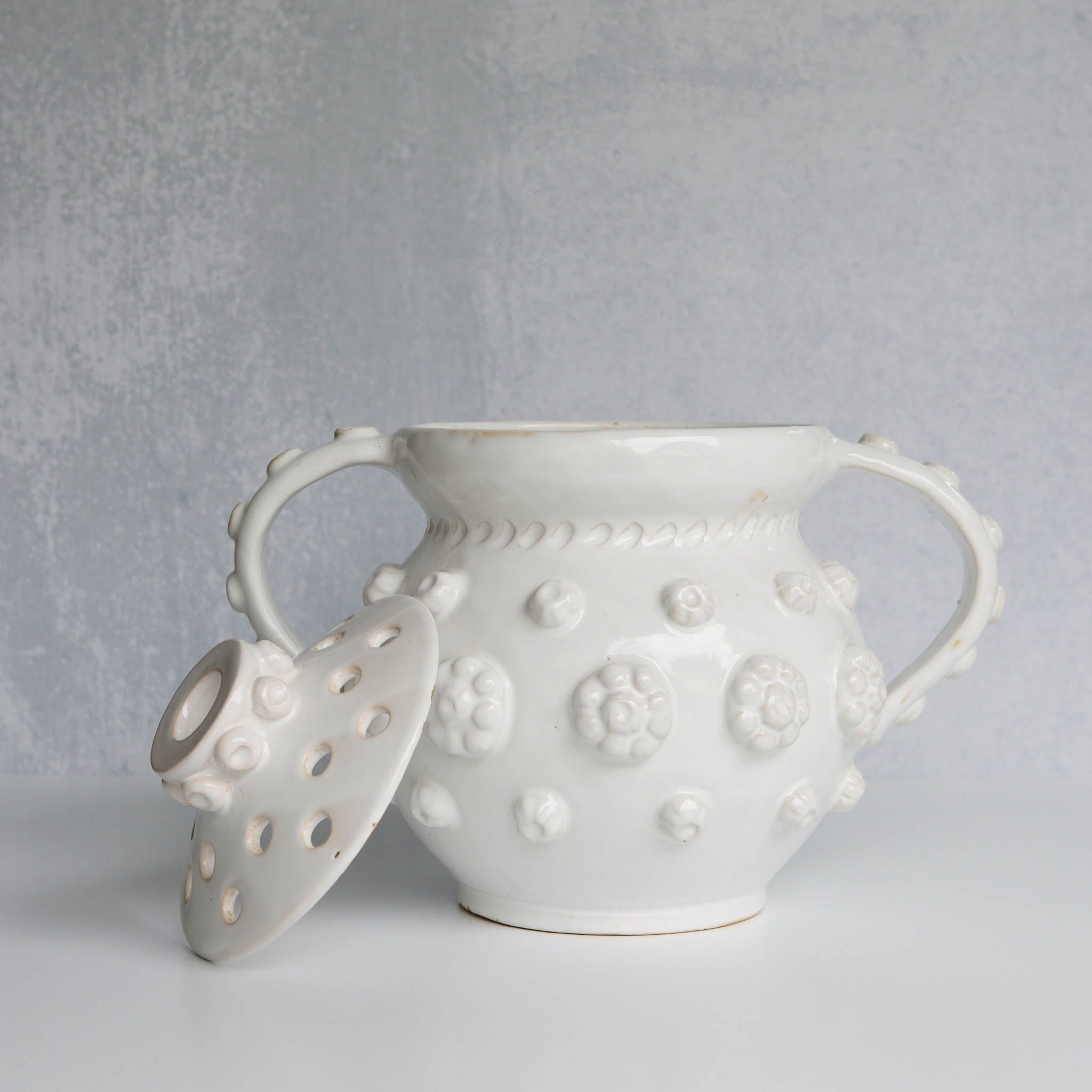 White ceramic vessel with removable lid with floral patterns on a gray background