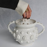 White textured ceramic vessel with handles held by a hand against a gray background