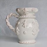 White ceramic pitcher with floral patterns and a rope handle on a gray background