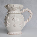 White ceramic pitcher with floral patterns and a twisted handle on a gray background