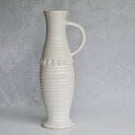 White ceramic pitcher with textured design and floral patterns on a gray background