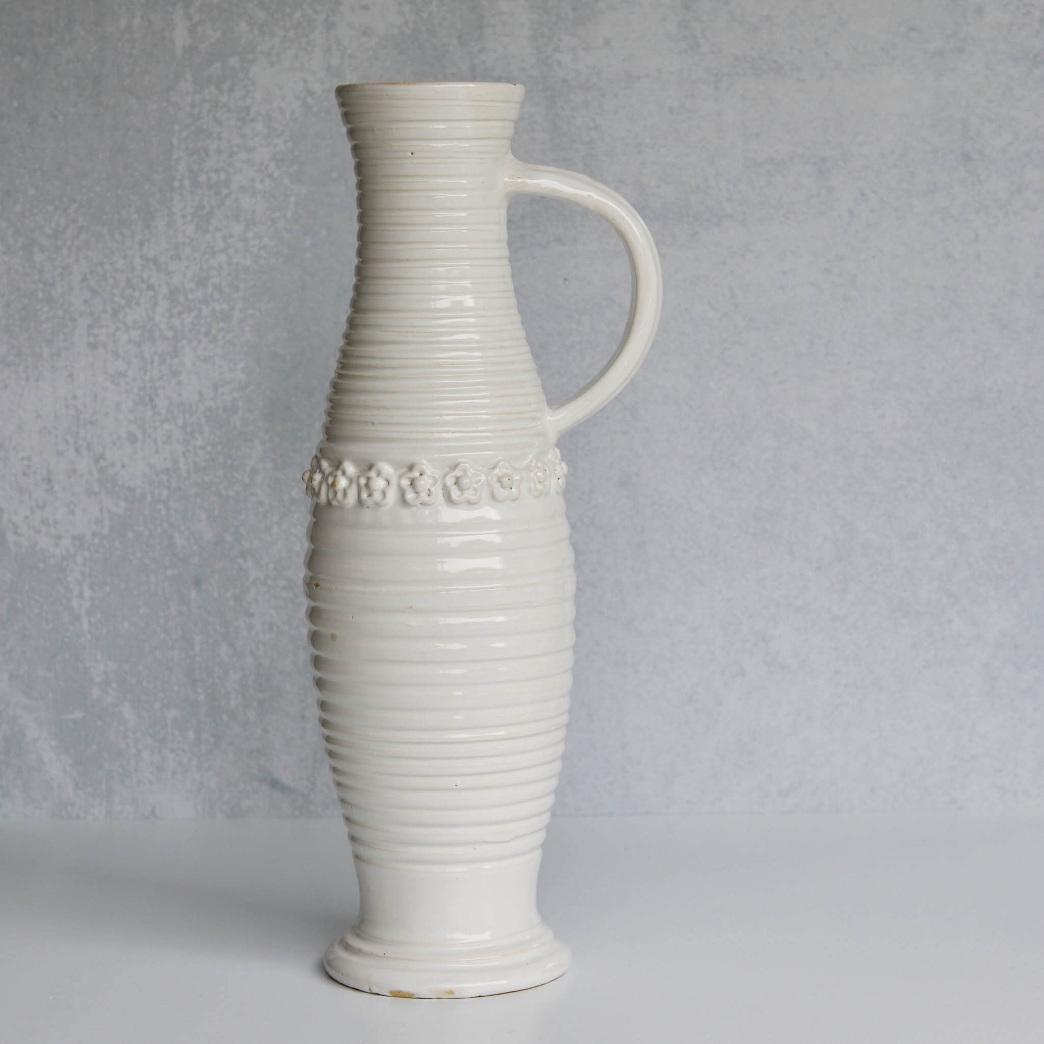 White ceramic pitcher with textured design and floral patterns on a gray background