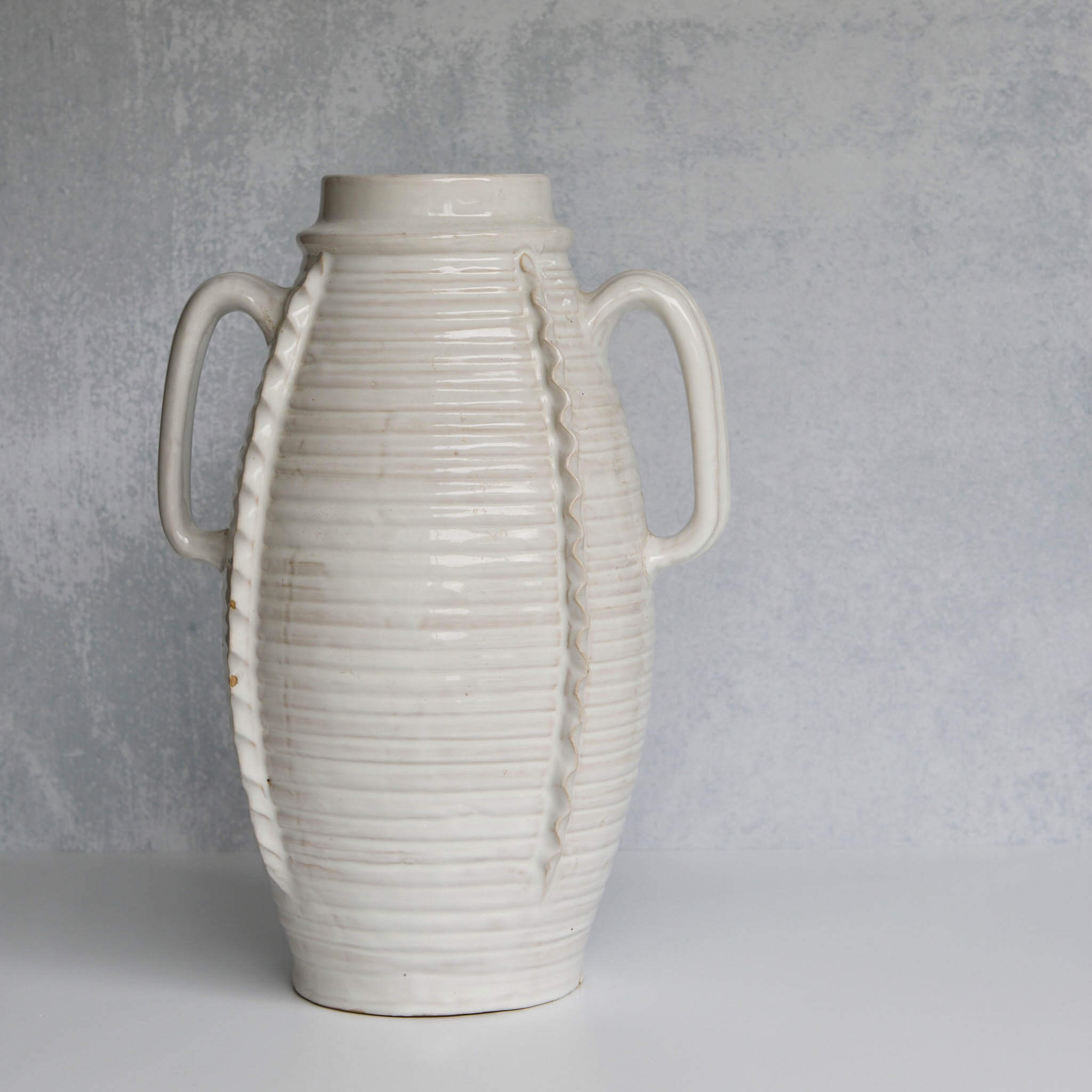 White ceramic vase with ribbed texture and handles on a gray background