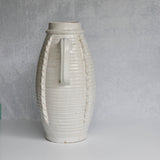 White ceramic vase with textured surface and handle on a gray background