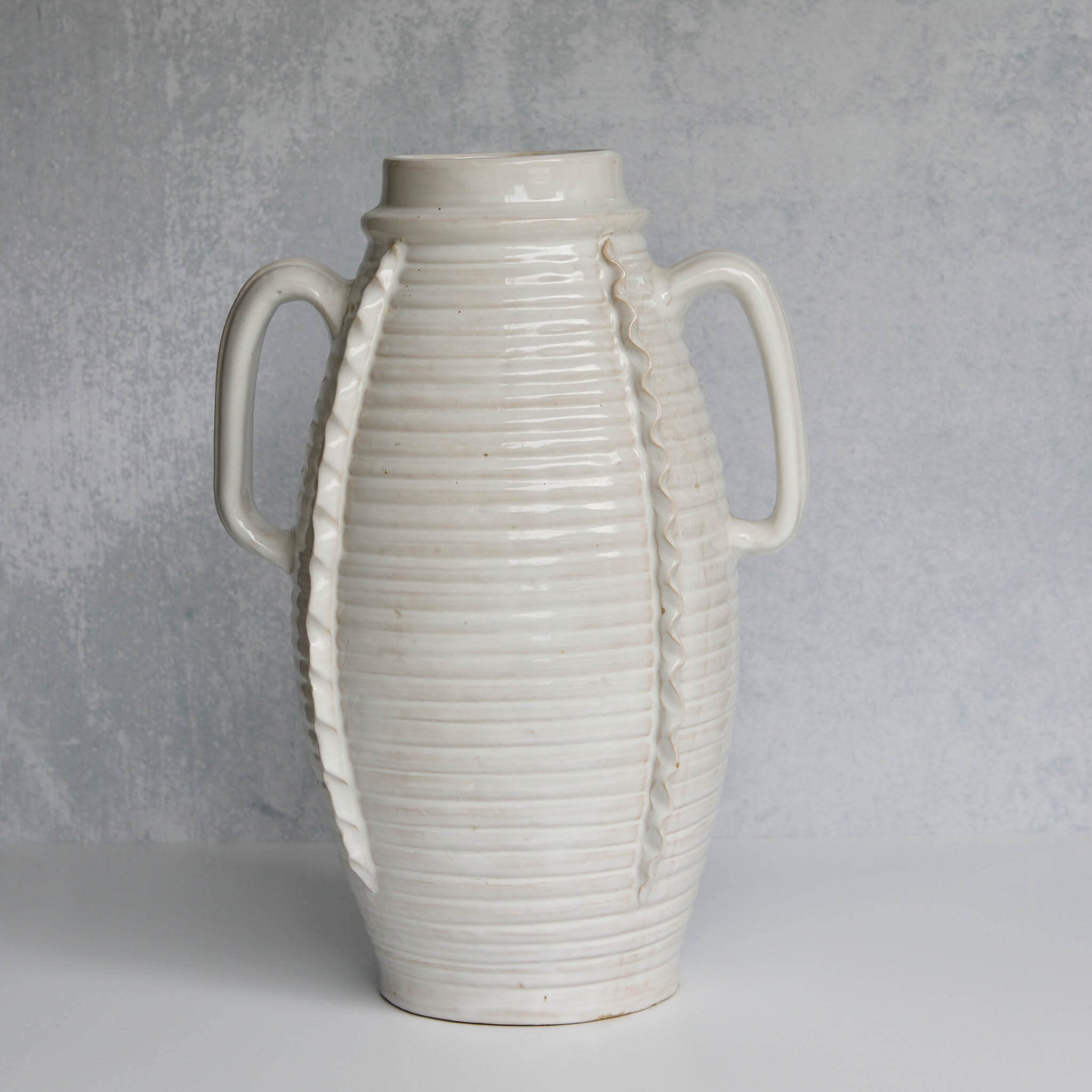 White ceramic vase with ribbed texture and handles on a gray background