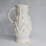 White ceramic handled pitcher with decorative patterns on a gray background