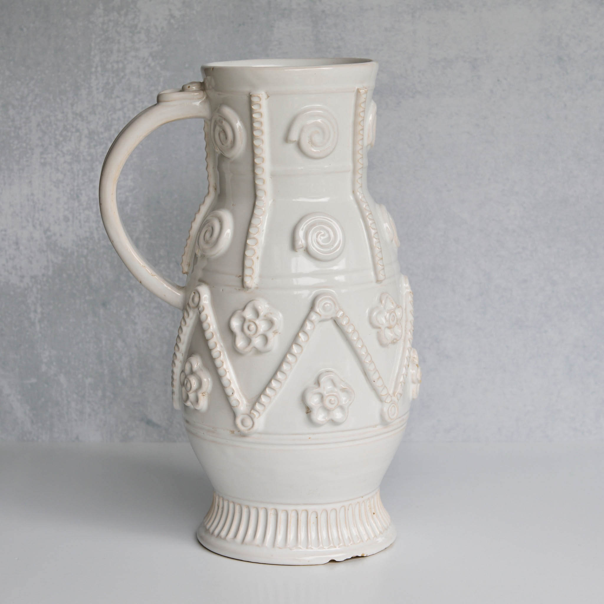 White ceramic handled pitcher with decorative patterns on a gray background