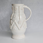 Decorative white ceramic pitcher with intricate patterns on a gray background