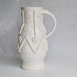 Decorative white ceramic pitcher with intricate patterns on a gray background