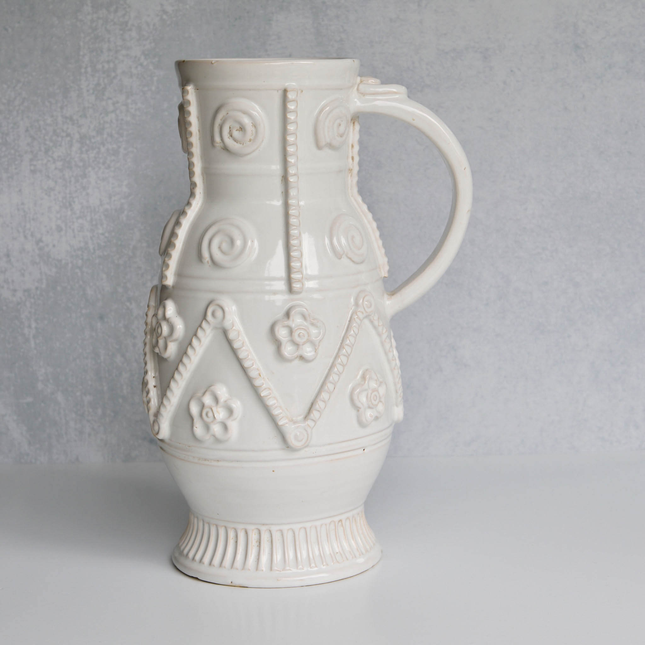 Decorative white ceramic pitcher with intricate patterns on a gray background