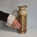 Person holding a ceramic Malarmey pitcher with decorative patterns against a gray background