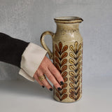 Person holding a ceramic Malarmey pitcher with decorative patterns against a gray background
