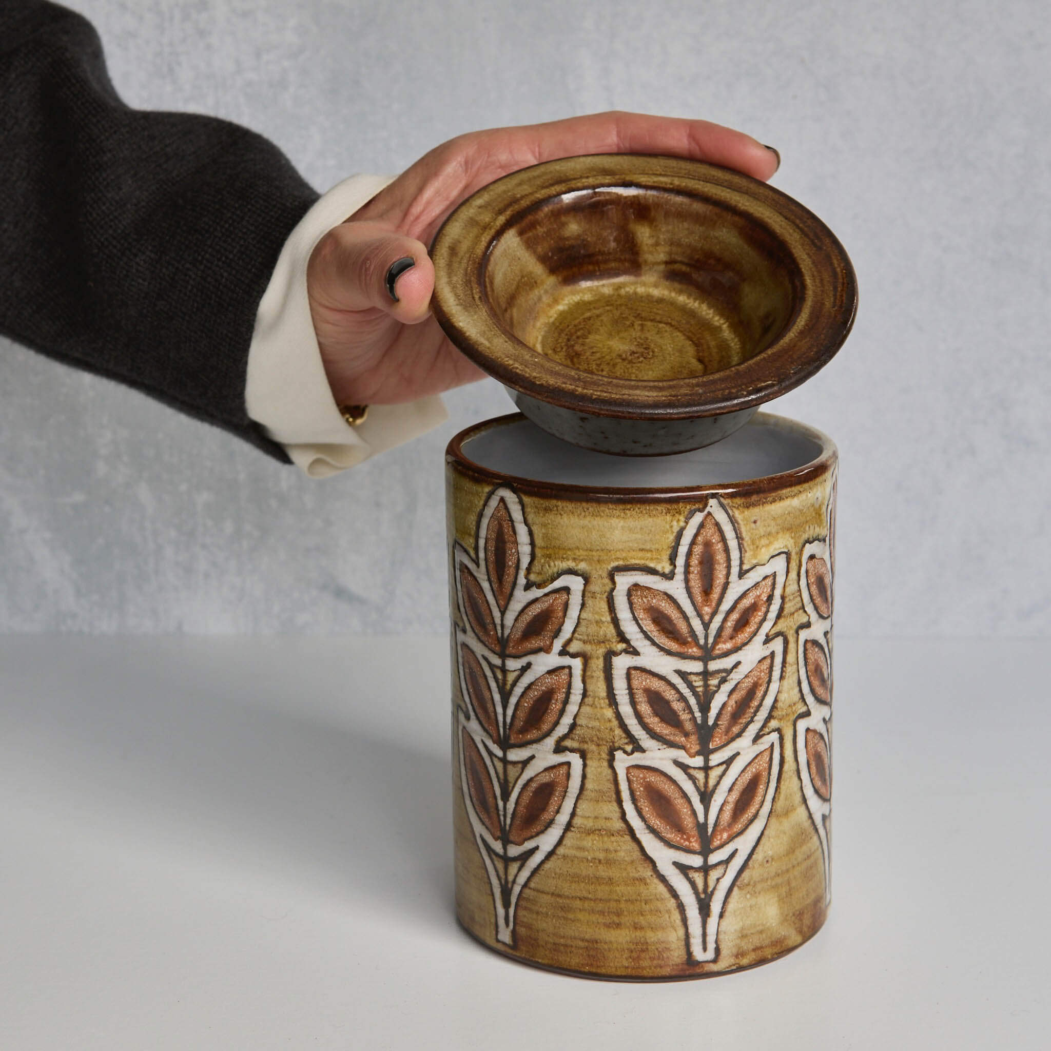Ceramic Malarmey lidded jar with lid featuring leaf patterns, held by a hand against a neutral background
