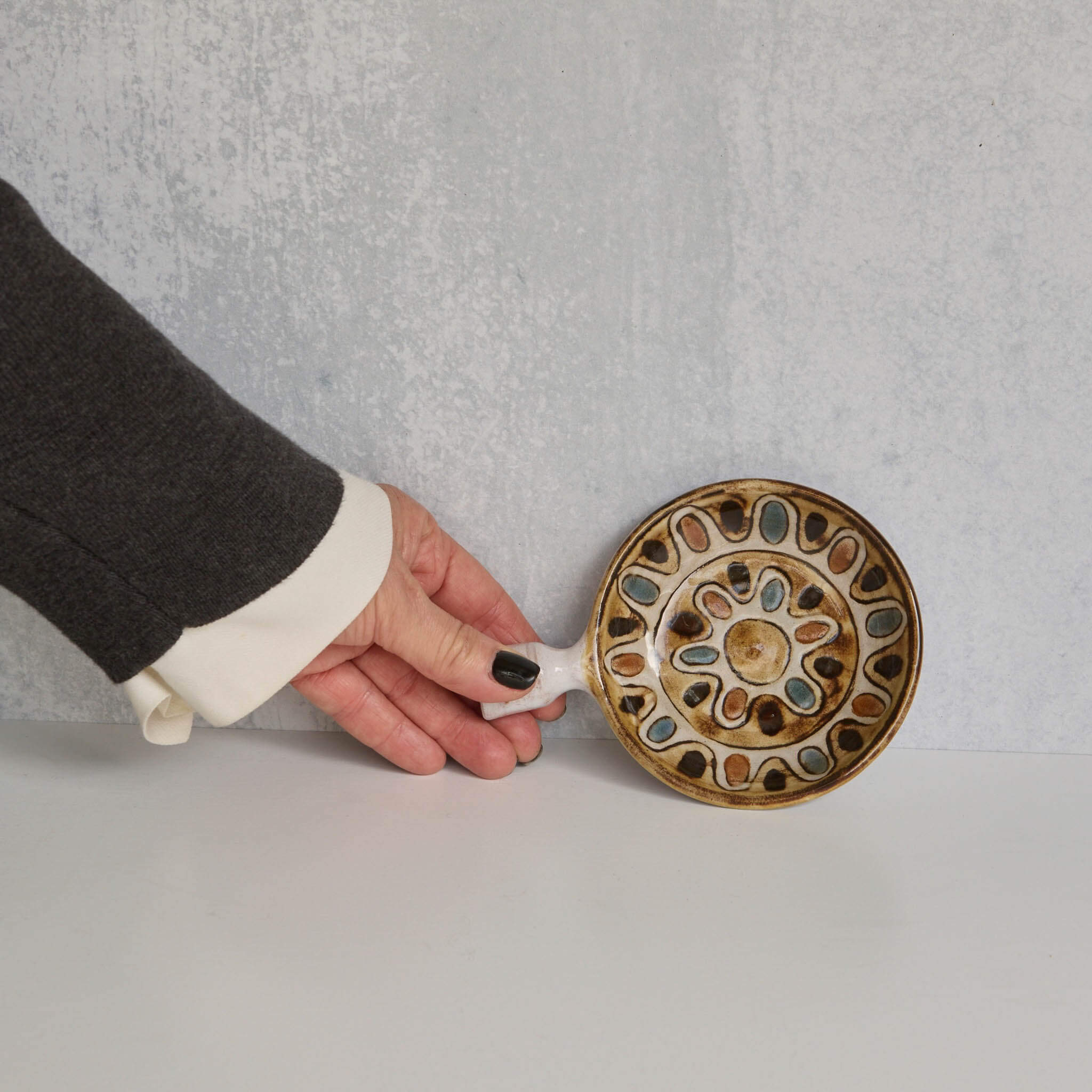 Ceramic dish with decorative handle held by a person against a gray background