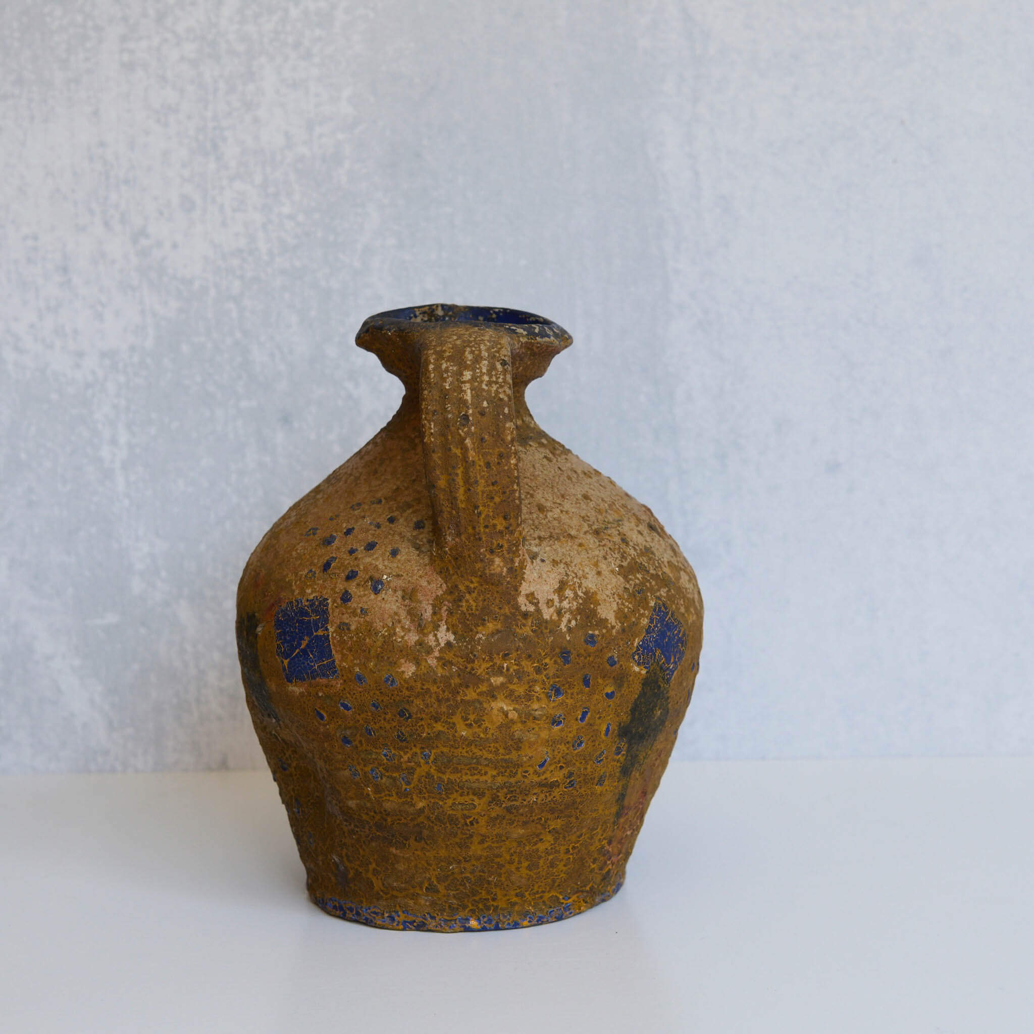 Brown stone pitcher with blue accents on a light gray background
