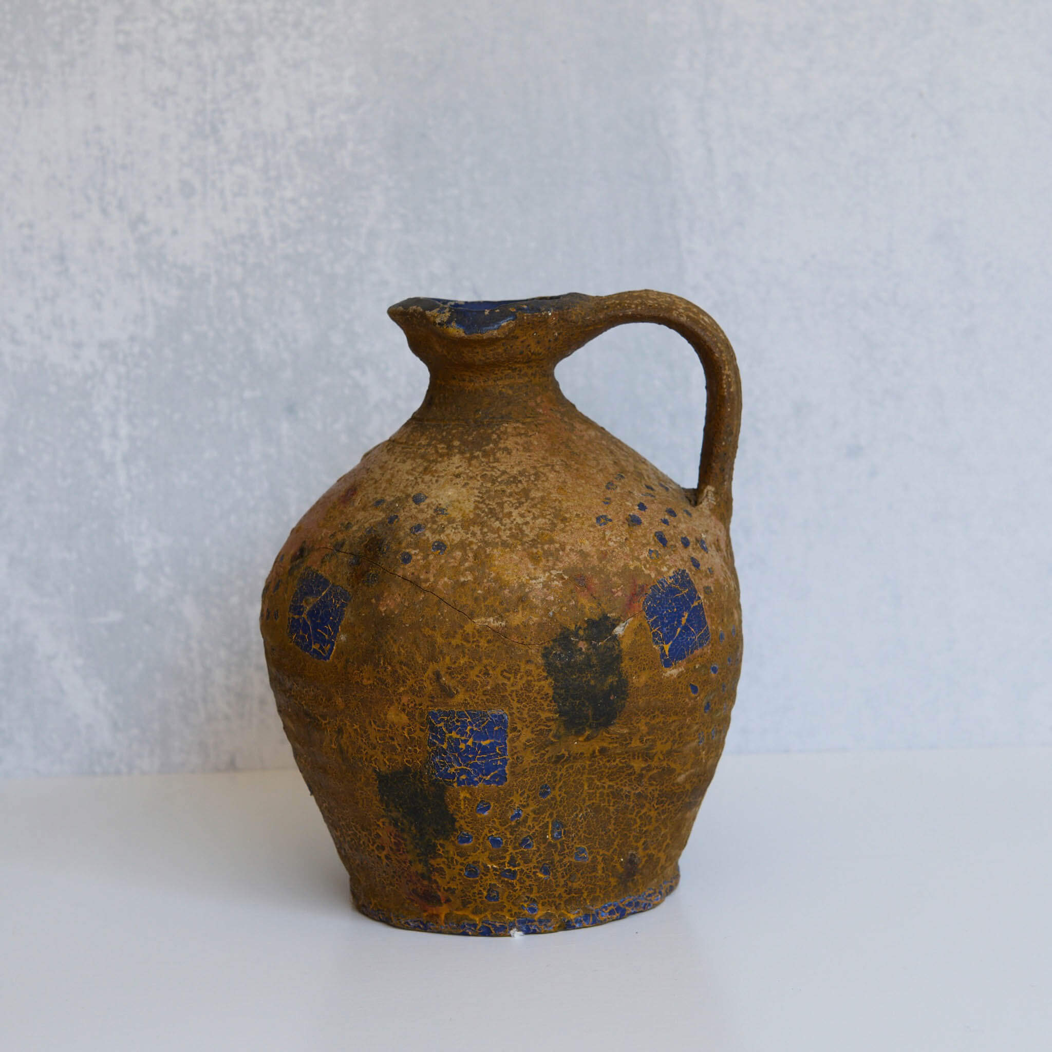 Brown stone pitcher with blue patterns on a light gray background
