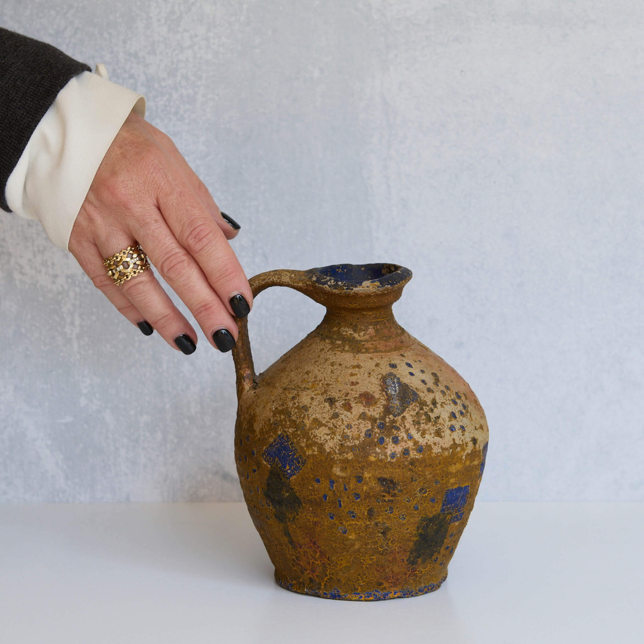 Person holding a rustic stone pitcher against a plain background