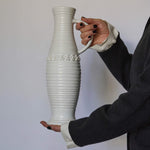 Person holding a tall white pitcher with textured design against a plain background