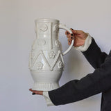 Person holding a decorative white ceramic pitcher against a plain background