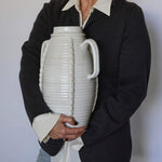 Person holding a large white ceramic vase against a plain background