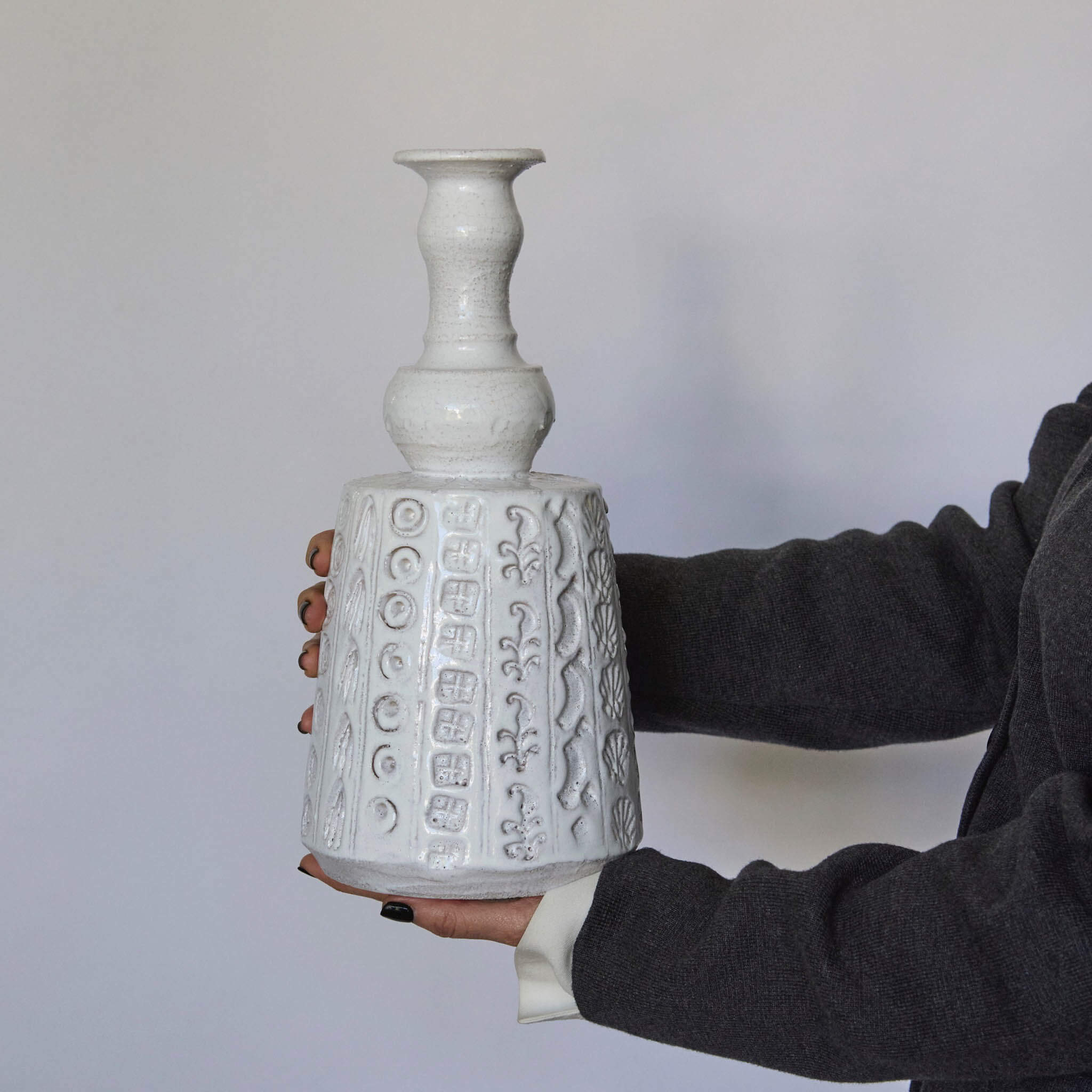 Person holding a textured white ceramic vase against a plain background