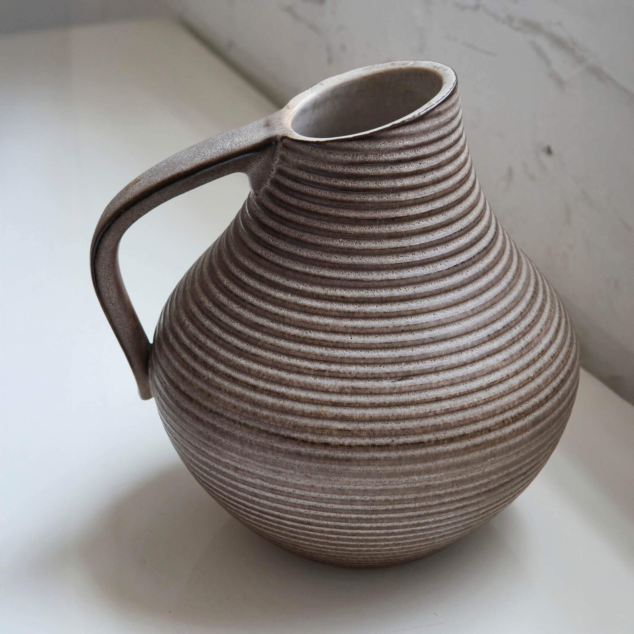 Stoneware pitcher with ribbed texture on a light background