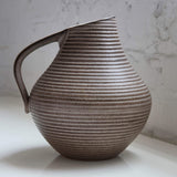 Stoneware pitcher with ribbed texture on a white surface and light gray background